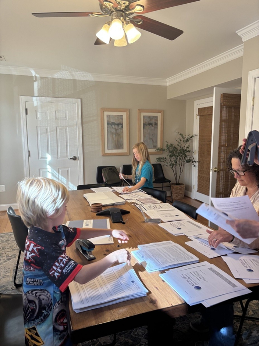 A woman and two children sorting stacks of printed documents