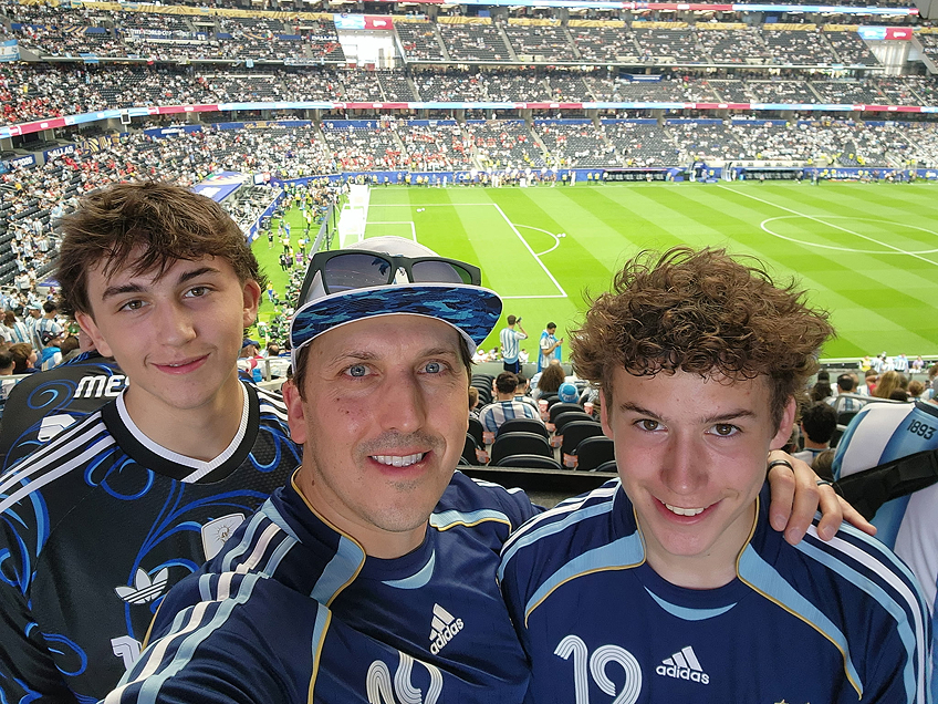 Father with teen children wearing soccer jerseys taking a selfie in a stadium