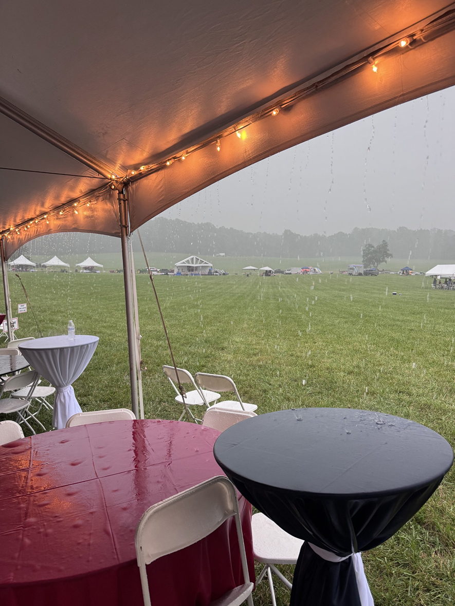 Rain falls on an outdoor tented event area with tables and chairs