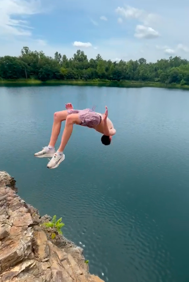 Coleman mid-backflip off rocky cliff into a lake with trees